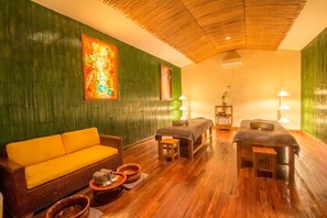 A room with a green wall, a wooden ceiling, a sofa, two foot massage tables, and a painting.