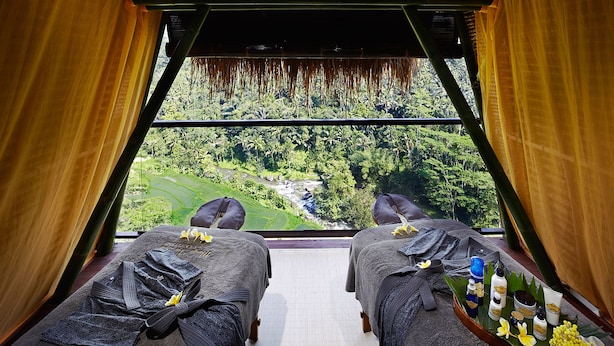 A room with two massage beds, a tray with toiletries, and a view of a lush landscape.