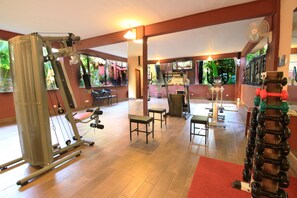 A gym with exercise equipment, wooden flooring, and large windows with views of greenery.