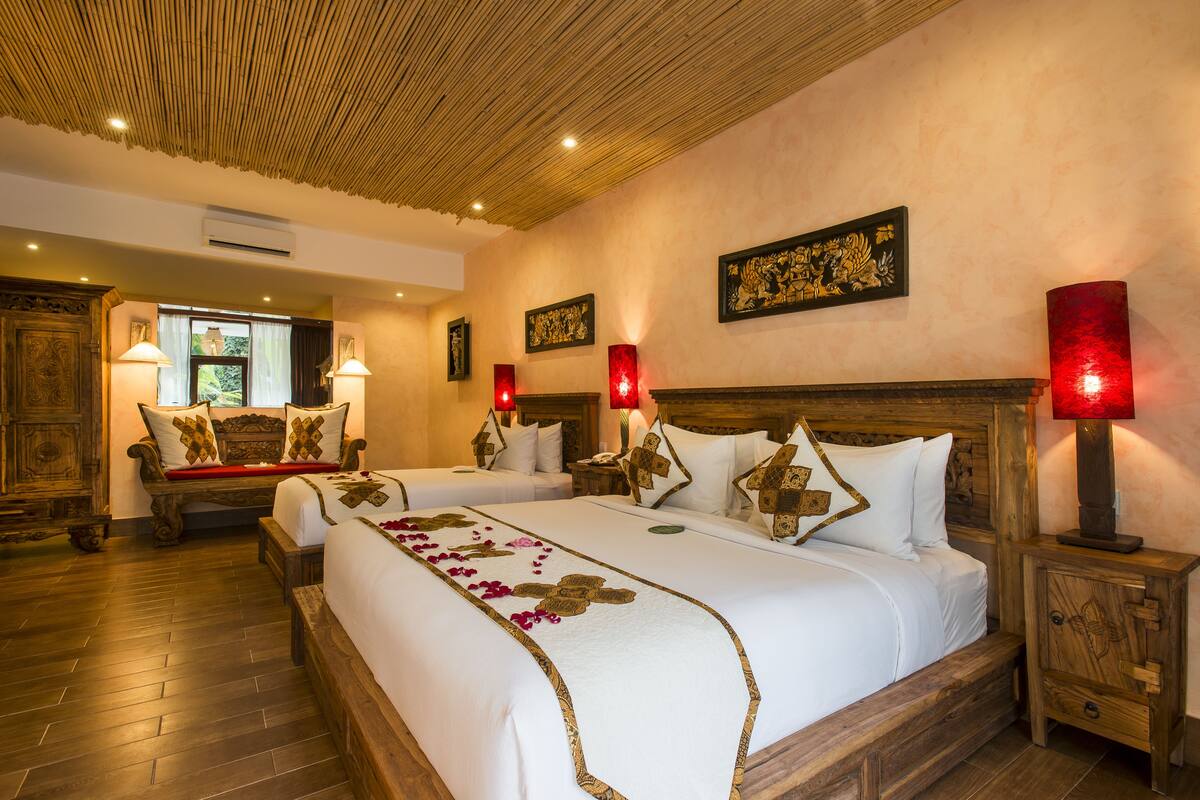 A hotel room with a large bed, two bedside tables with lamps, a wooden bench, and a wall with framed artwork.