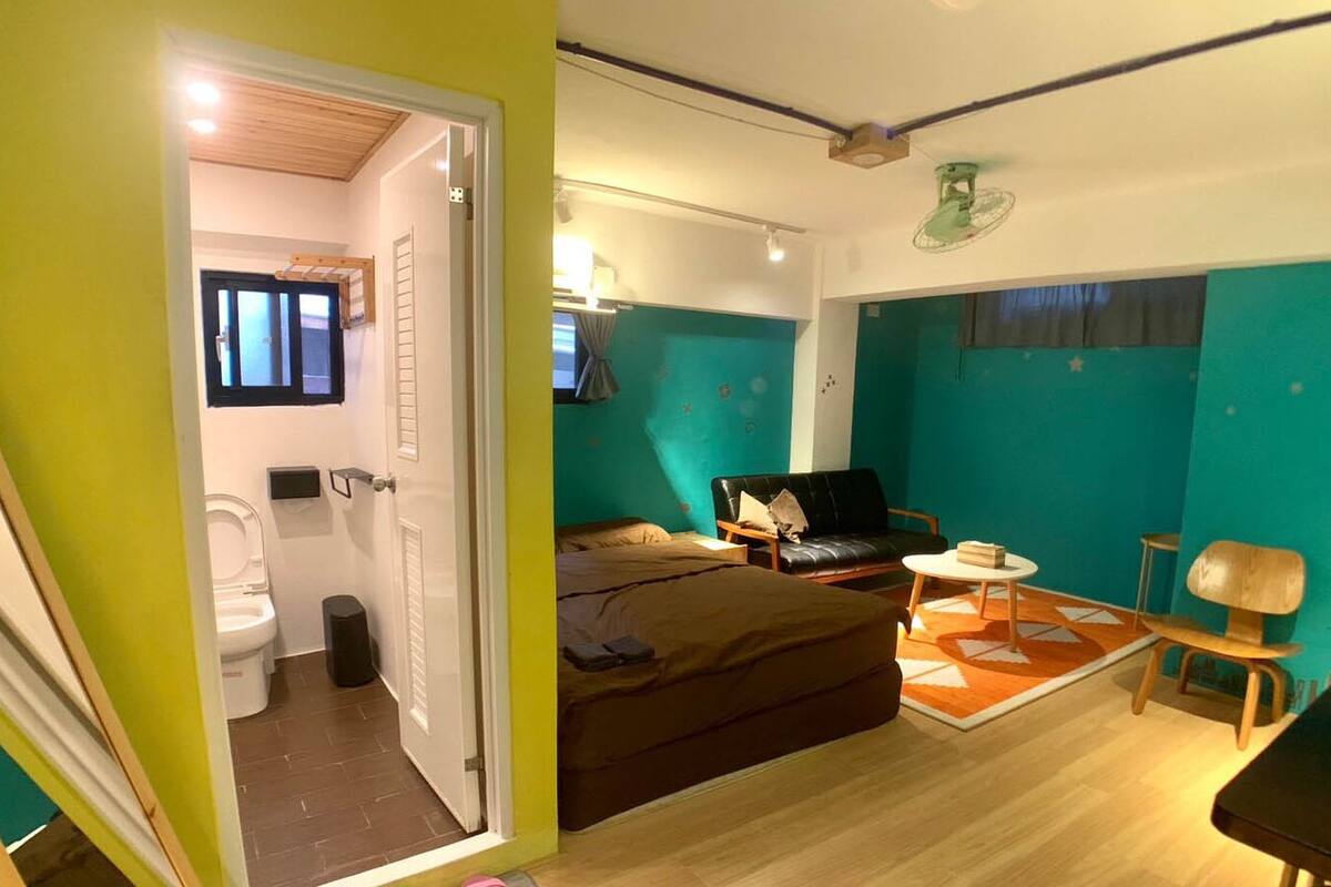 A compact hotel room with a bed, a small table, a chair, and a bathroom visible through an open door.