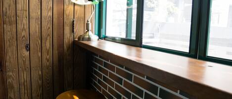 A corner with a wooden wall, a brick wall, and a window with a view of buildings outside.
