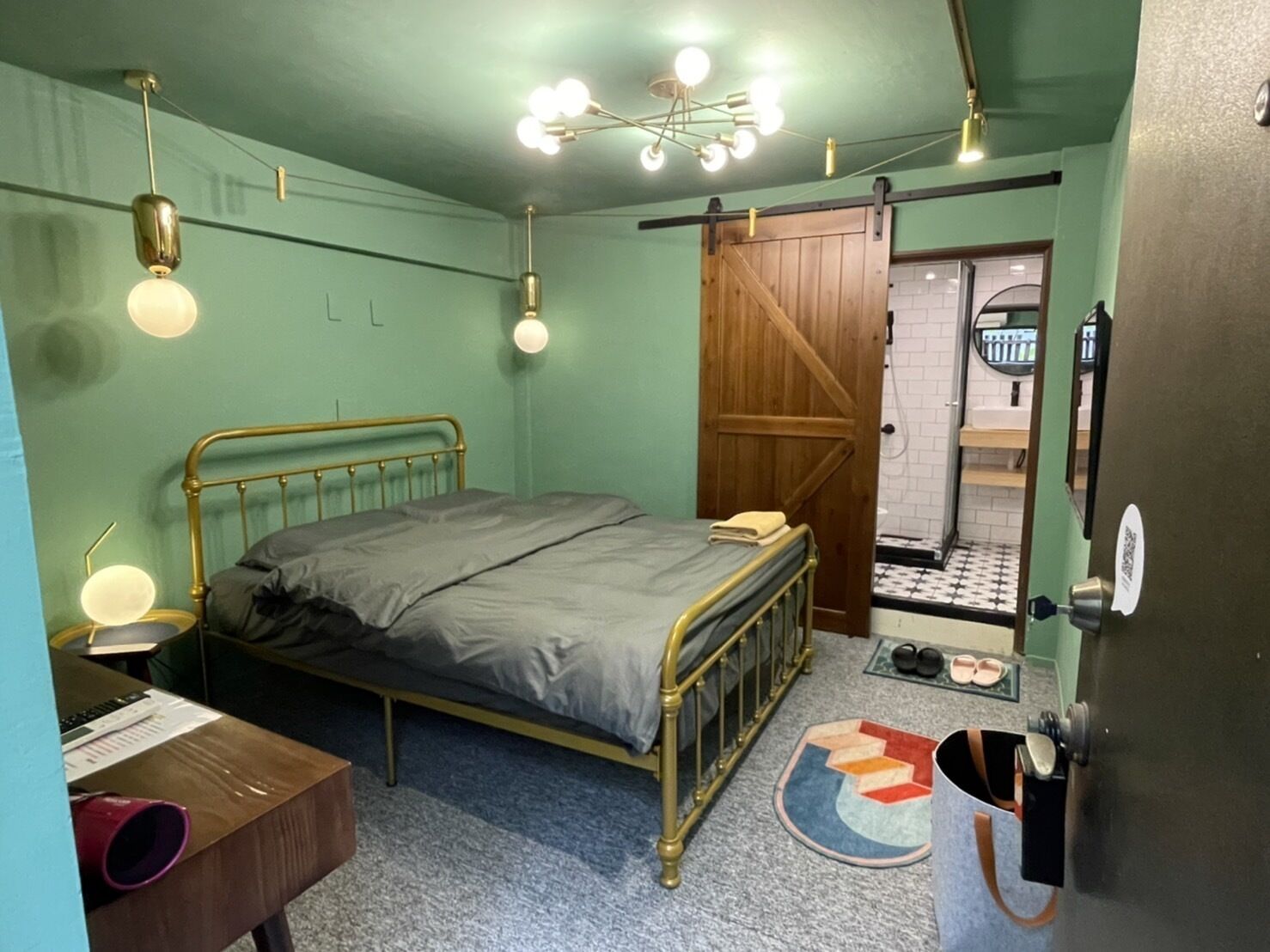 A bedroom with a bed, a desk, a chair, a wardrobe, and a bathroom visible through an open door.