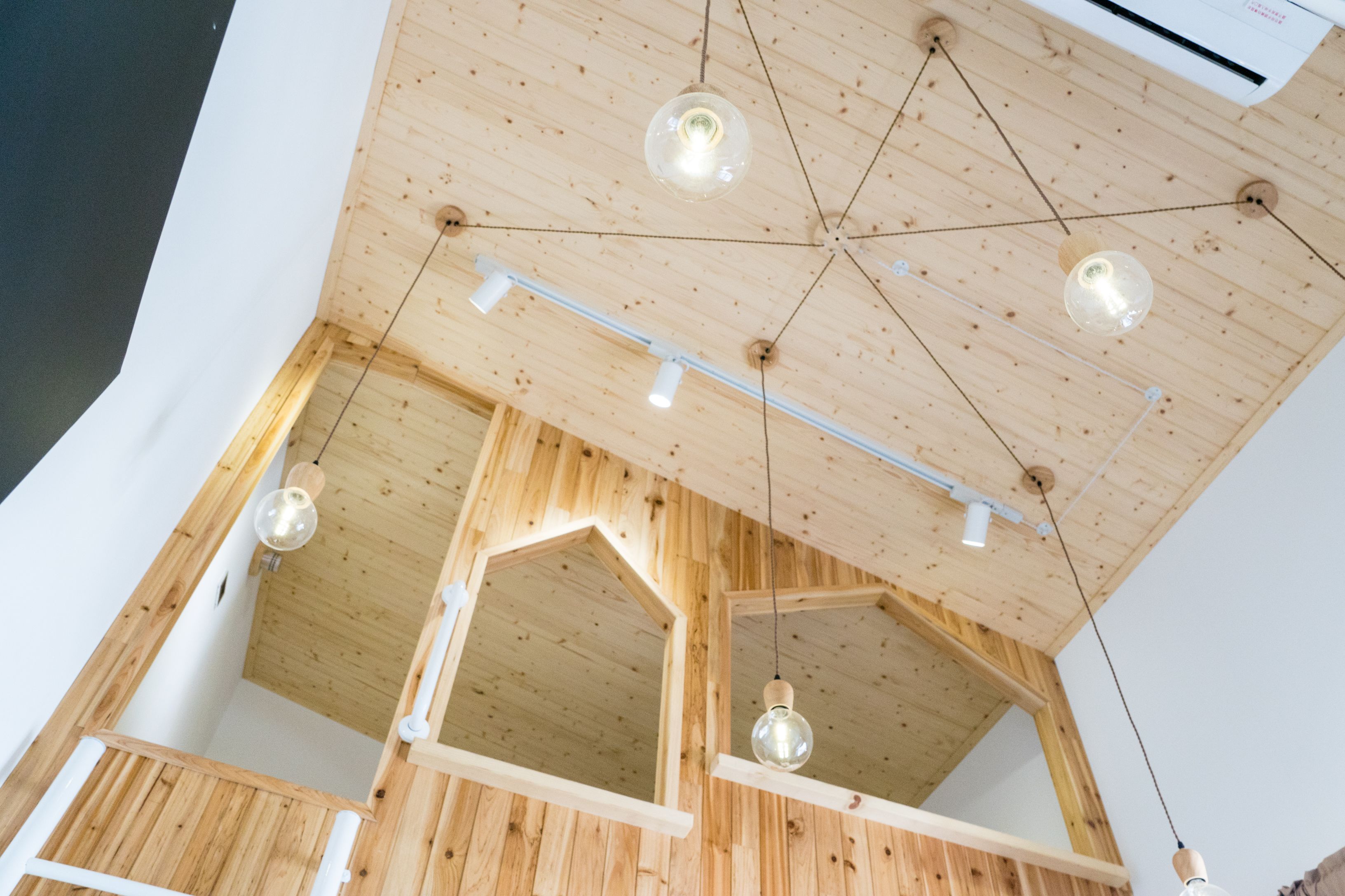 A room with wooden walls and ceiling, multiple hanging light fixtures, and a visible air conditioning unit.