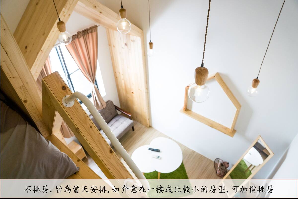 A room with a sloped ceiling, wooden beams, a bed, a small round table, and hanging pendant lights.