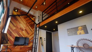 A modern interior with a wooden floor, a black door, a mounted TV, a ladder, a fan, and a table with a decorative item. - 日木民宿 (Tainan)