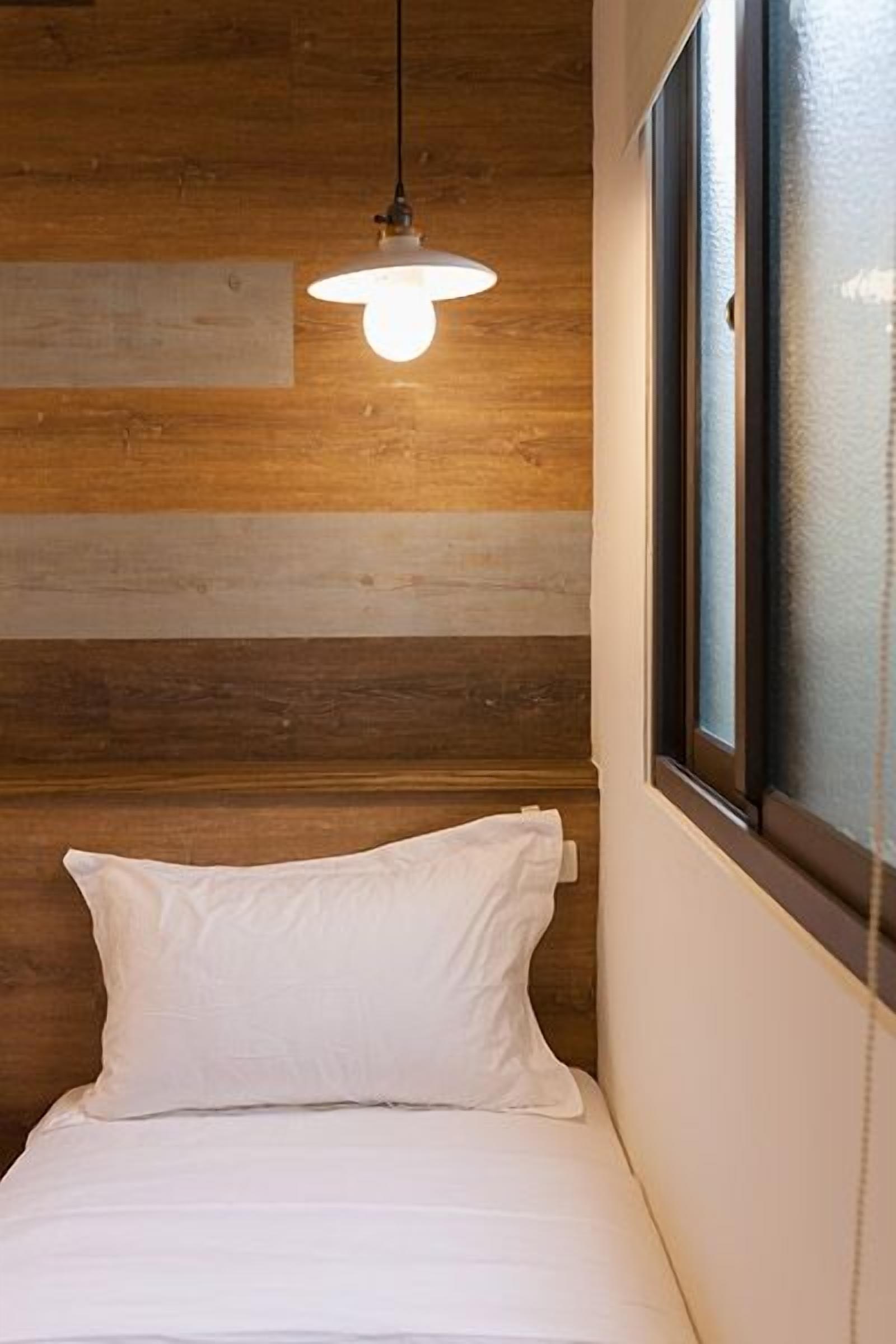 Cama de solteiro com roupa de cama branca num quarto com paredes de madeira e uma janela com vista.