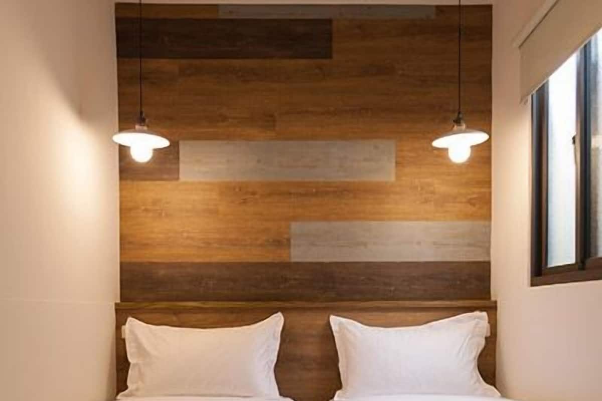 Quarto com duas camas, parede de painéis de madeira e iluminação pendente.