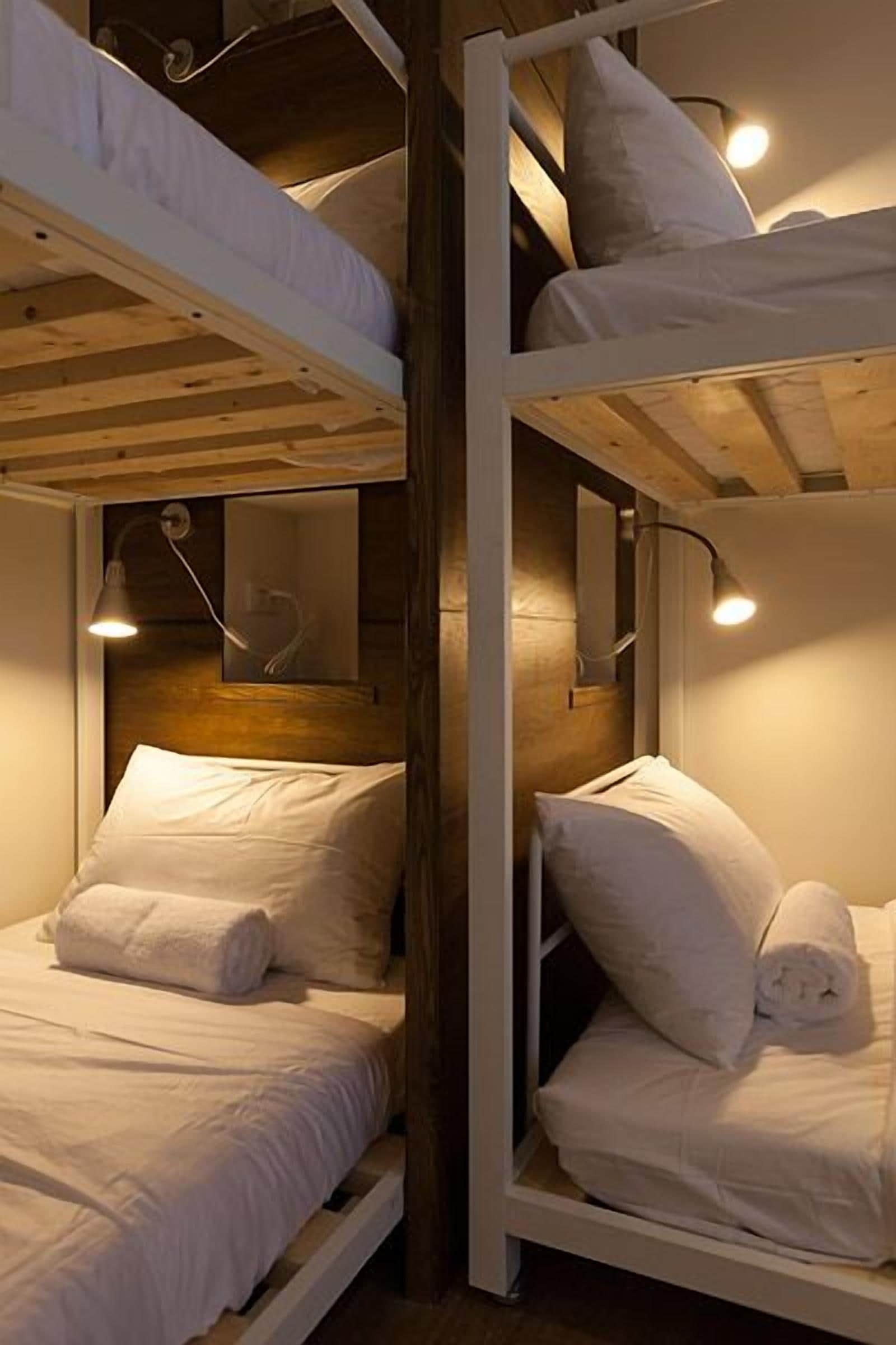 Habitación con literas, ropa de cama blanca y dos lámparas de noche.