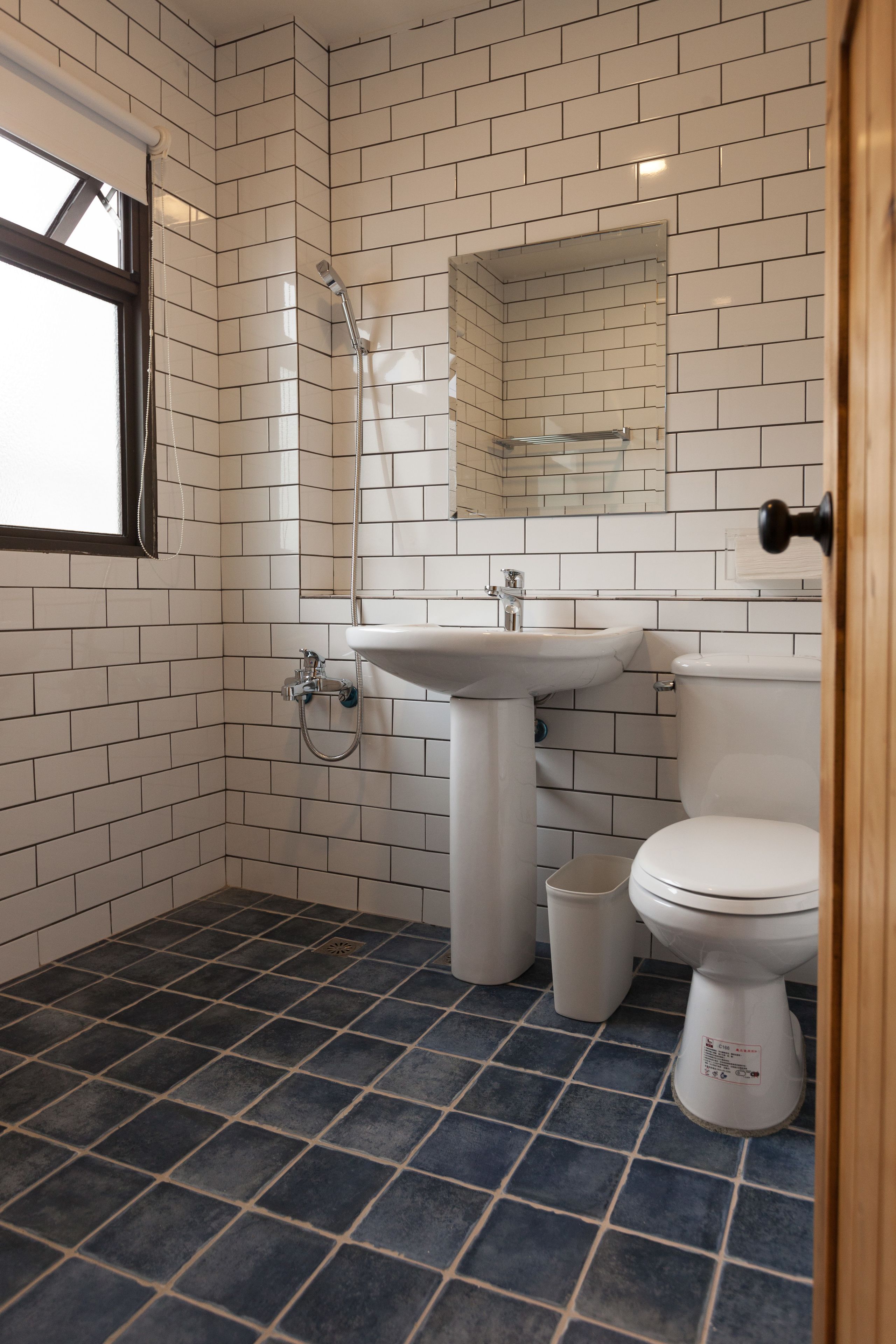 Et badeværelse med hvide flisevægge, en hvid vask, toilet og brusebad.
