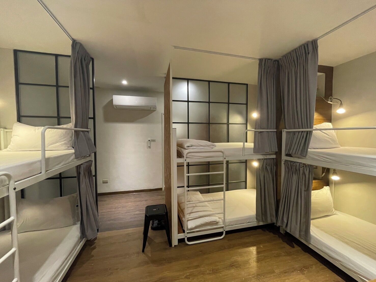 Een kamer met drie stapelbedden, een klein krukje en een airconditioning op de muur.
