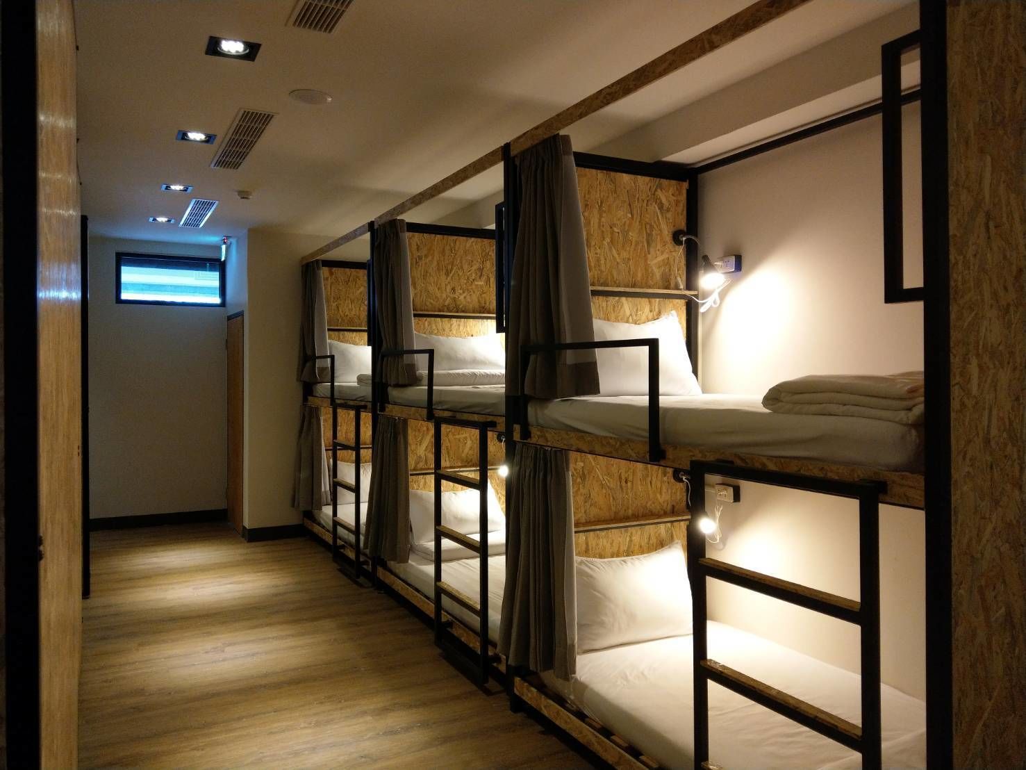 A corridor with bunk beds, wooden walls, and a ceiling with recessed lighting.