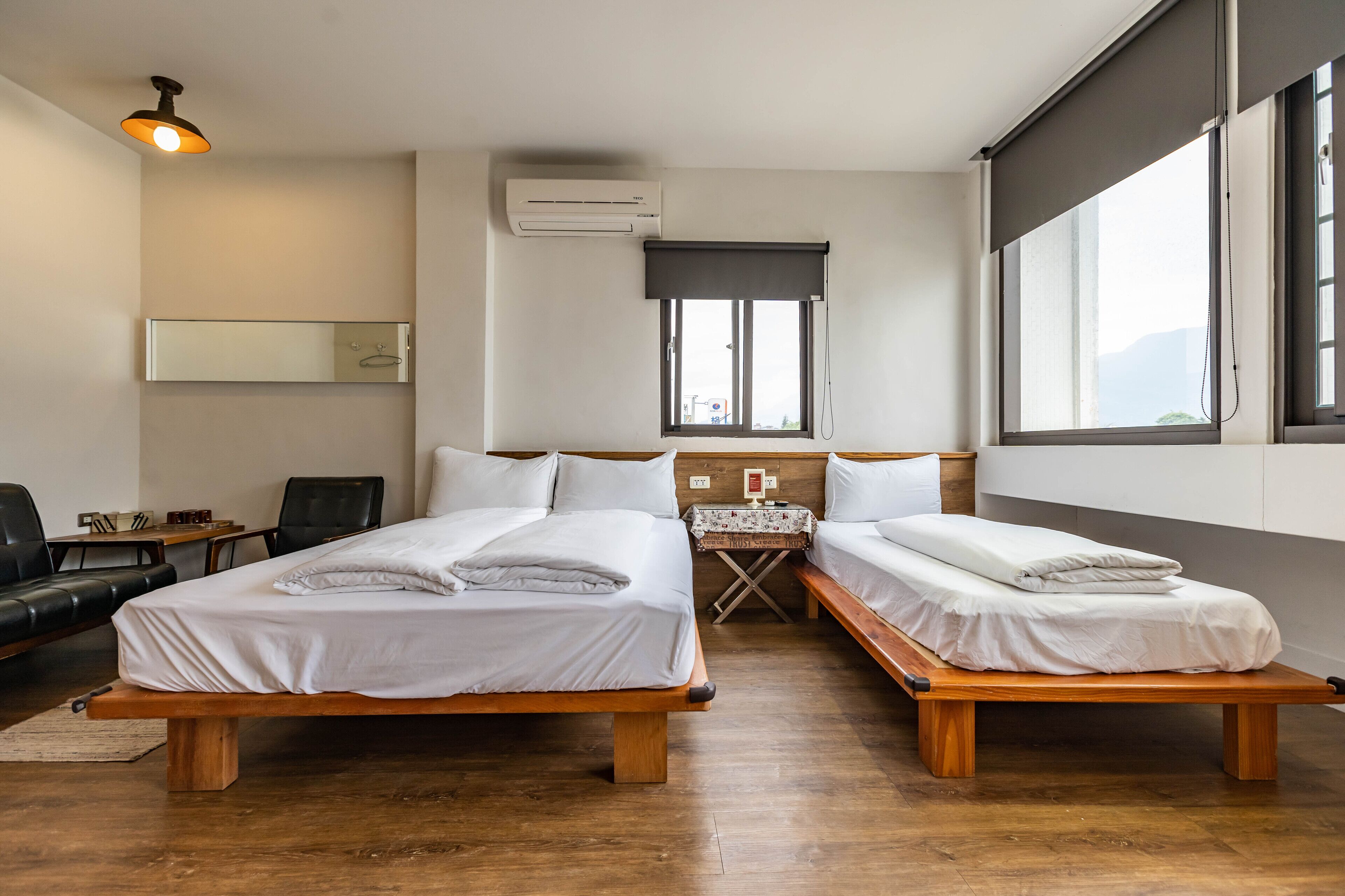 A hotel room with two beds, a desk, a chair, a table, and a window.