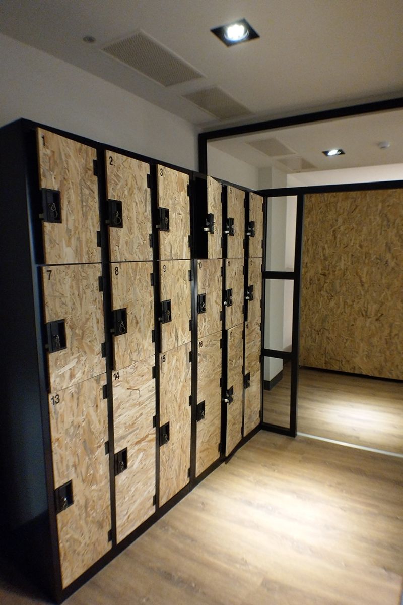Une rangée de casiers, chacun portant un numéro, un plancher en bois et une porte donnant sur une autre pièce.