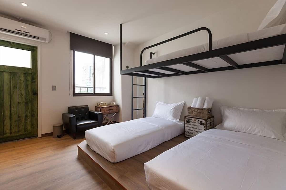 Quarto com duas camas de solteiro, uma cama beliche, uma escrivaninha, uma cadeira e uma janela.