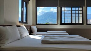Habitación de hotel con cama, almohadas y vistas a las montañas a través de amplios ventanales.