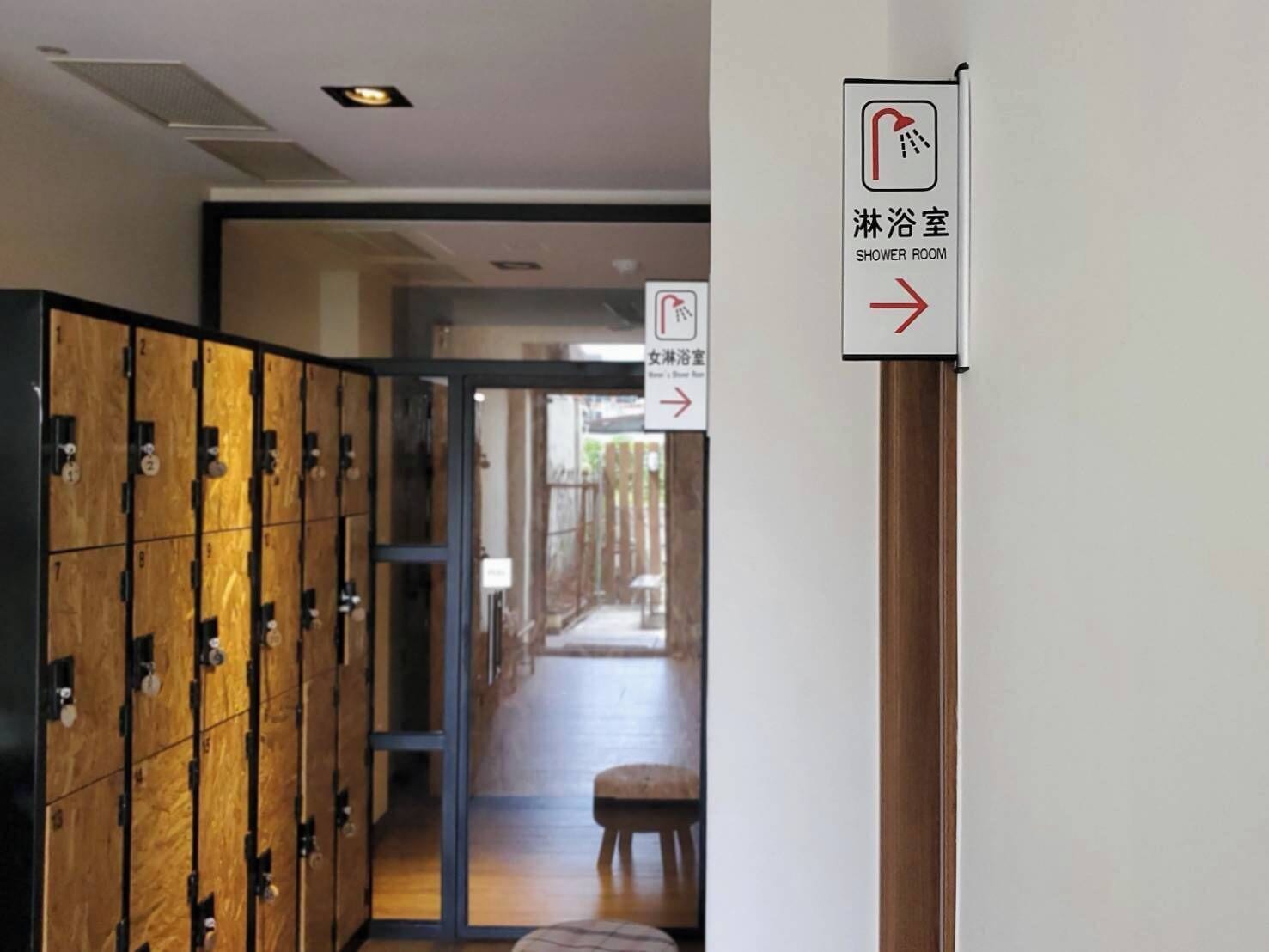 A hotel corridor with wooden lockers, a shower room sign, and a directional arrow.