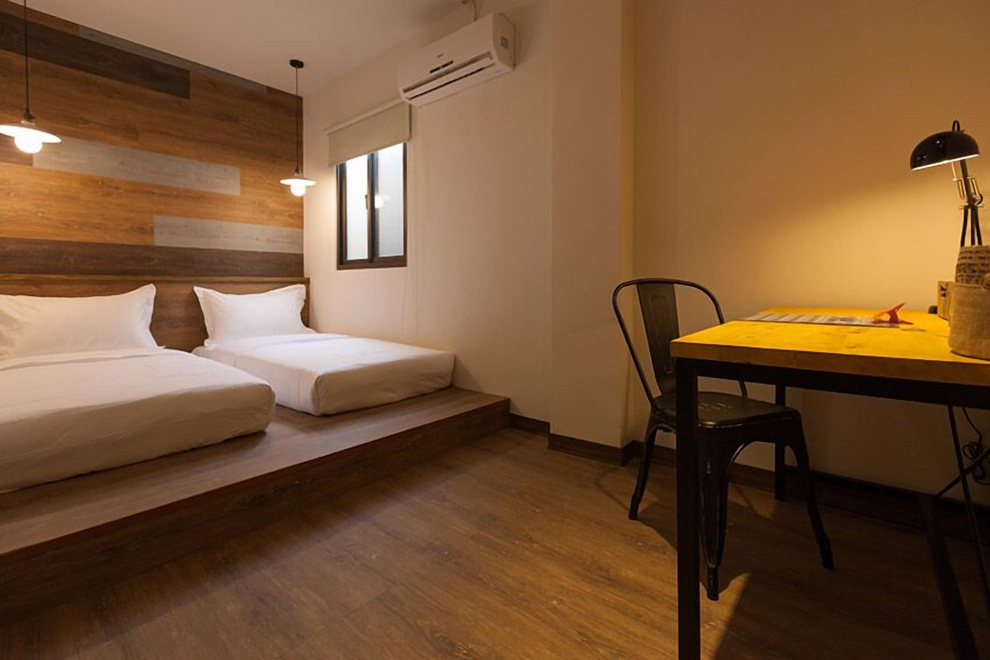 A room with a bed, a desk, and a chair. There is a window and an air conditioning unit on the wall.