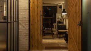 Un interior moderno con una puerta de madera, una pared de ladrillo y una zona de comedor con mesa y sillas.