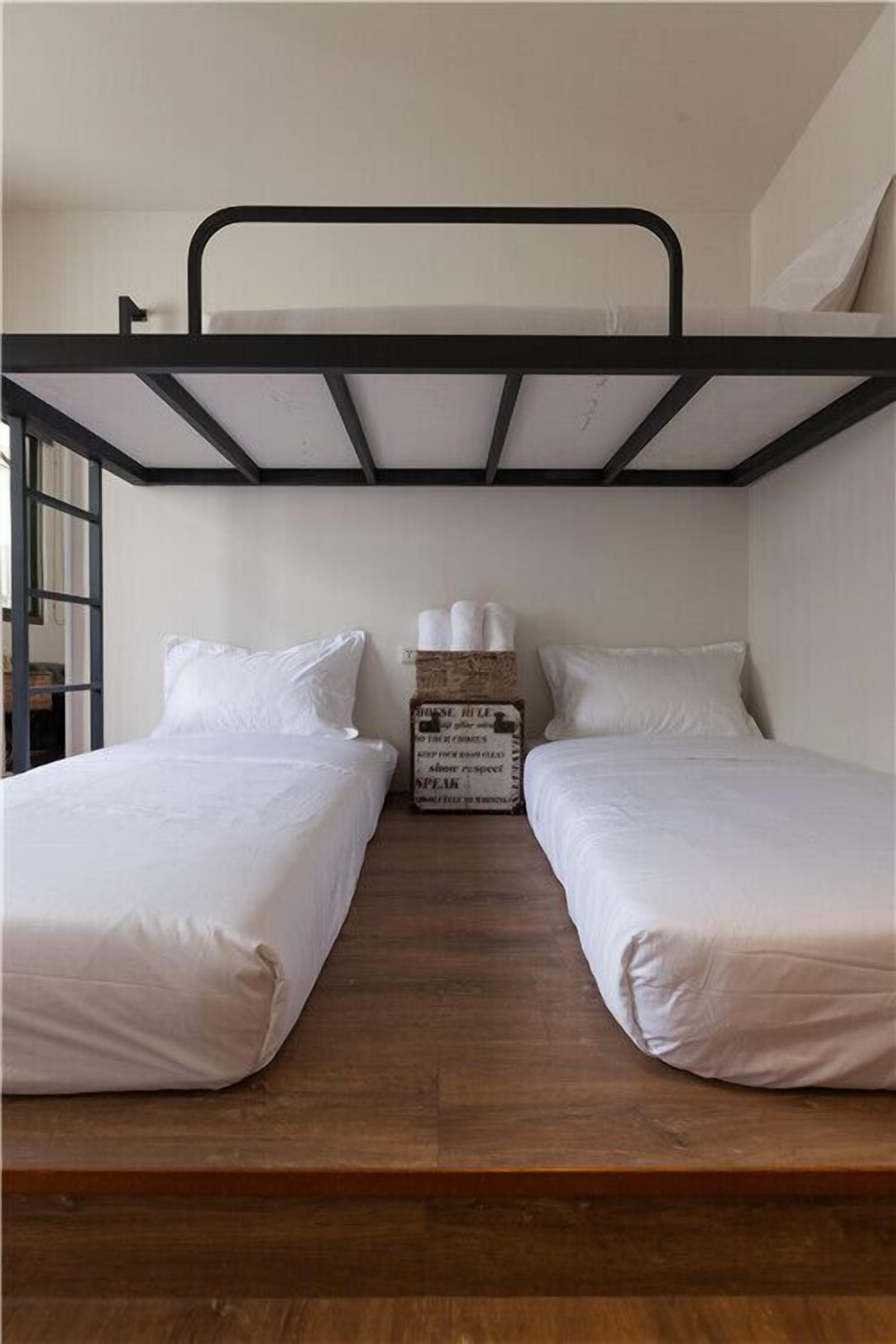A bunk bed room with two beds, a wooden floor, and a small table with a box of tissues.