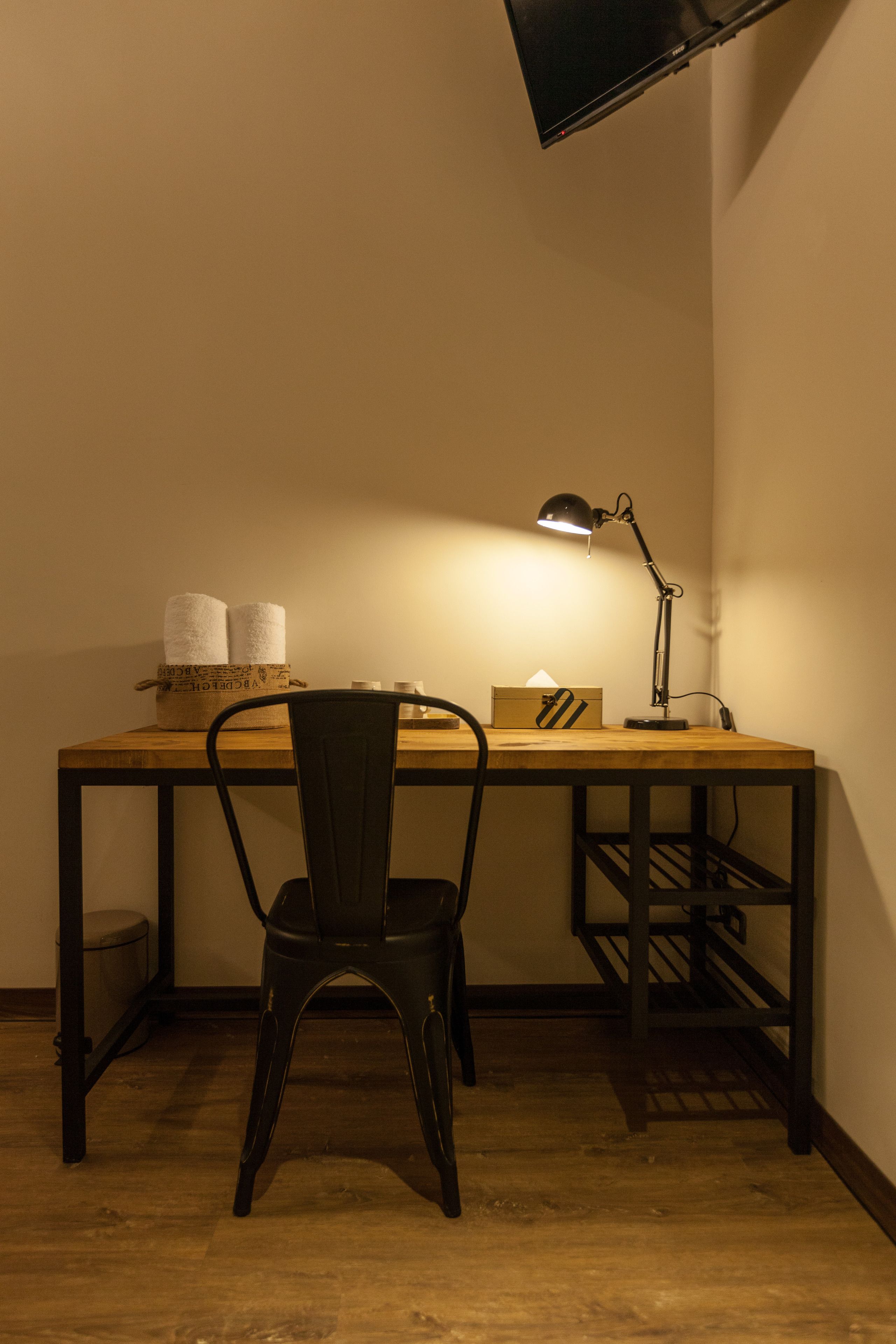 A small workspace with a wooden desk, a black chair, a desk lamp, and a box of tissues.