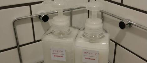 A bathroom with white tiled walls and a metal shelf holding two bottles of shampoo and body soap.