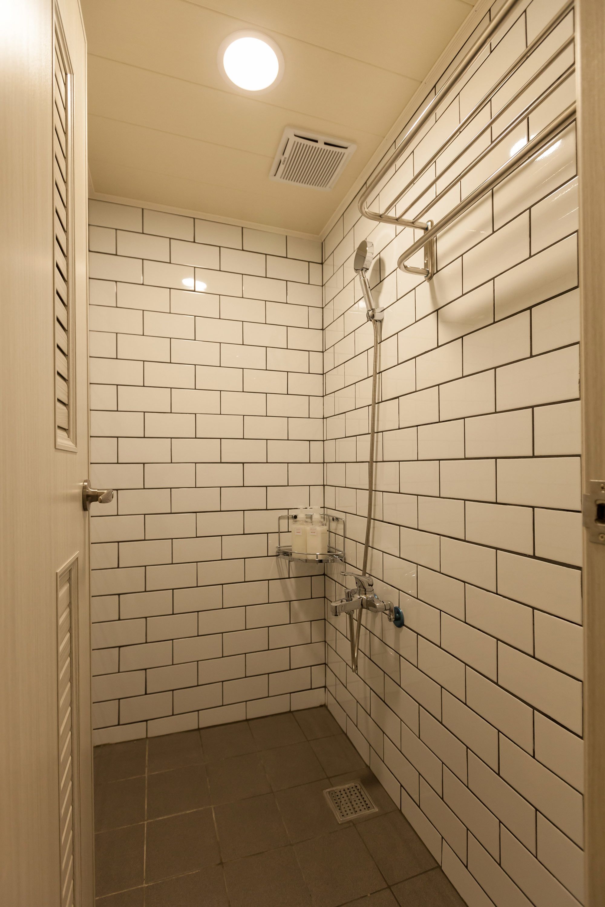 A small, tiled shower room with a showerhead and control panel.