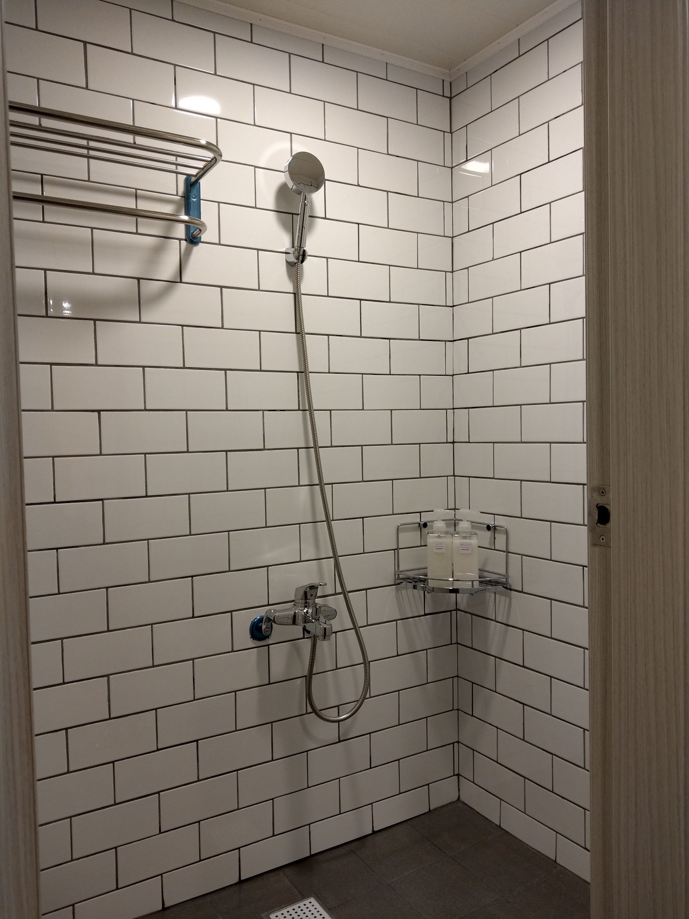 A small, tiled shower area with a handheld showerhead and a wall-mounted faucet.