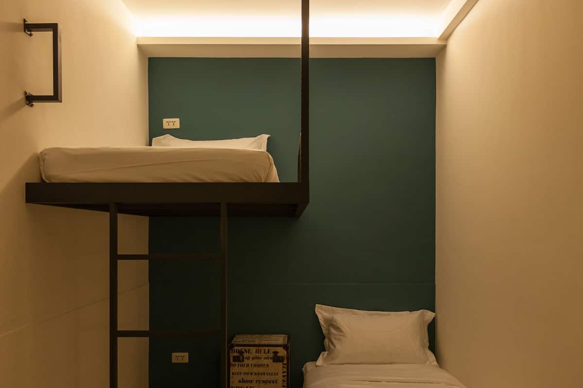 Quarto pequeno e estreito com beliche, uma cama de solteiro e soalho de madeira.