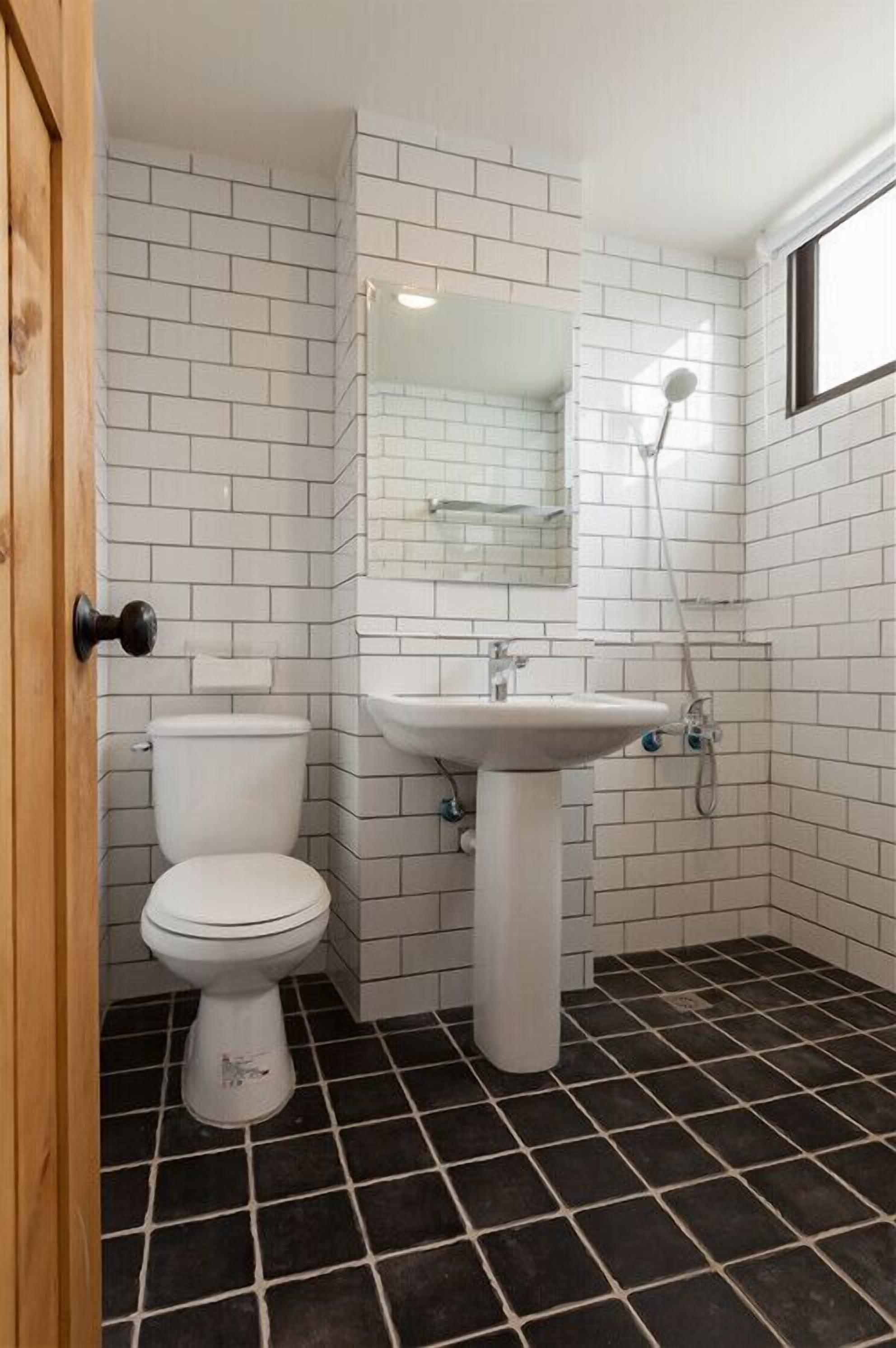 A bathroom with white tiled walls, a white toilet, a pedestal sink, and a shower.