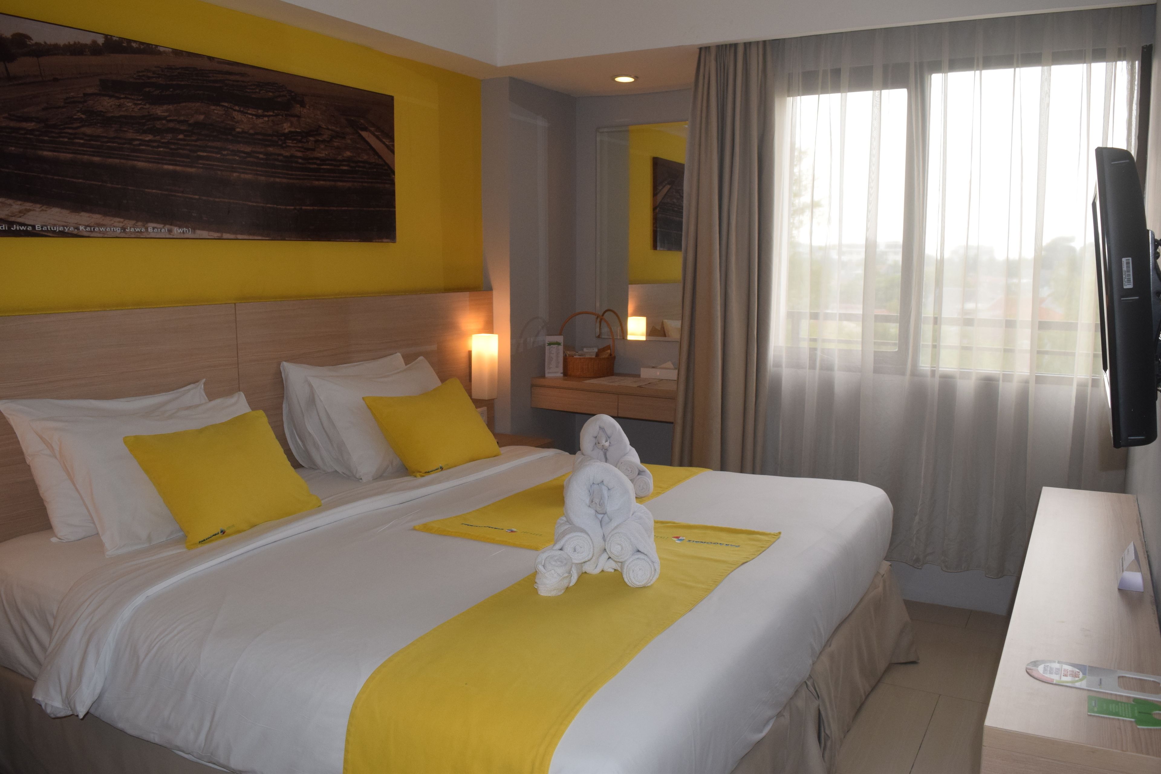 Habitación de hotel con una cama grande, una mesita de noche, un televisor y una ventana con cortinas.