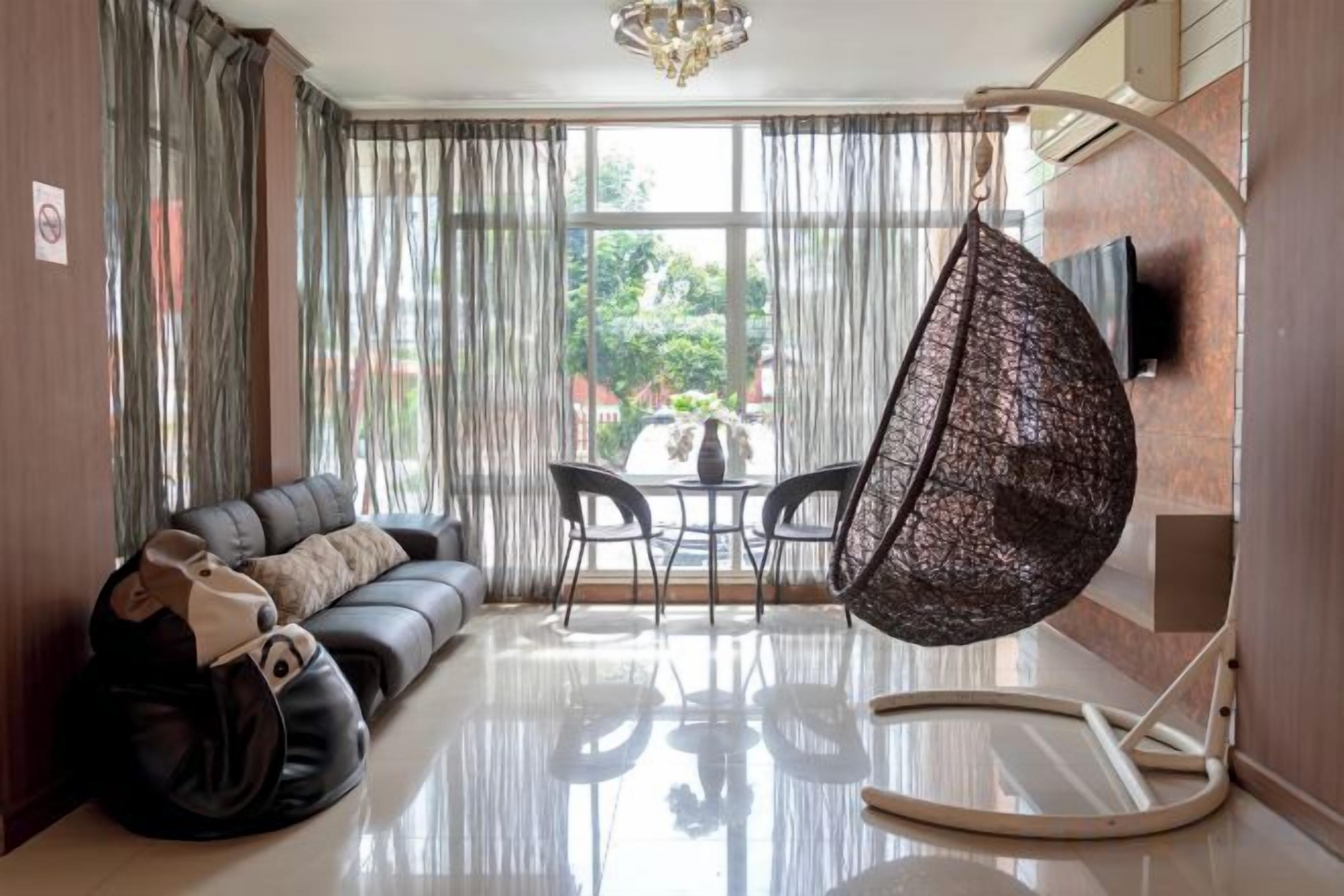 Ein modernes Wohnzimmer mit einer Couch, Sesseln, einem Hängekorbstuhl und Blick durch große Fenster.