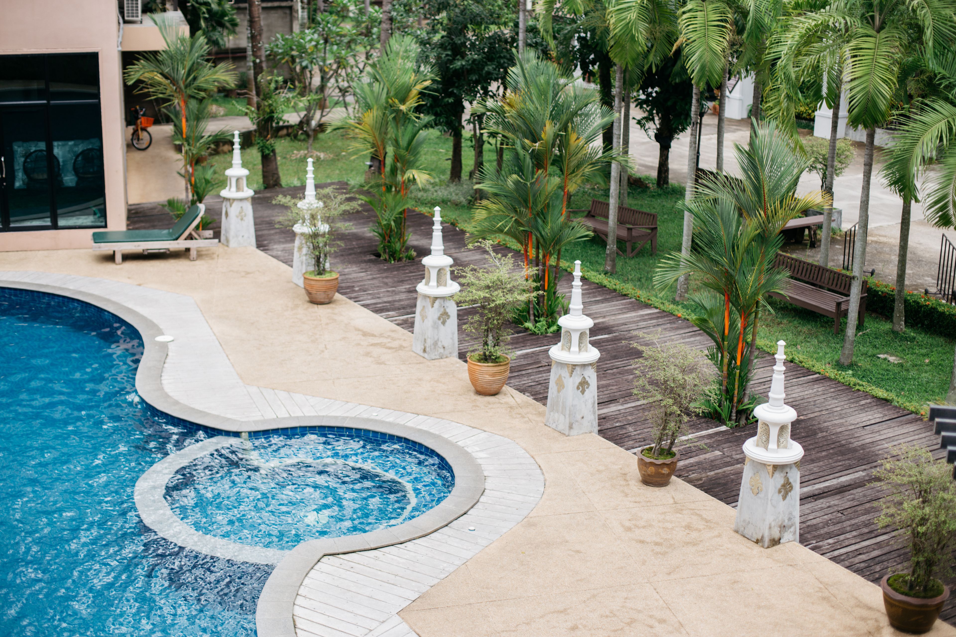A swimming pool with a wooden deck, surrounded by palm trees and benches.