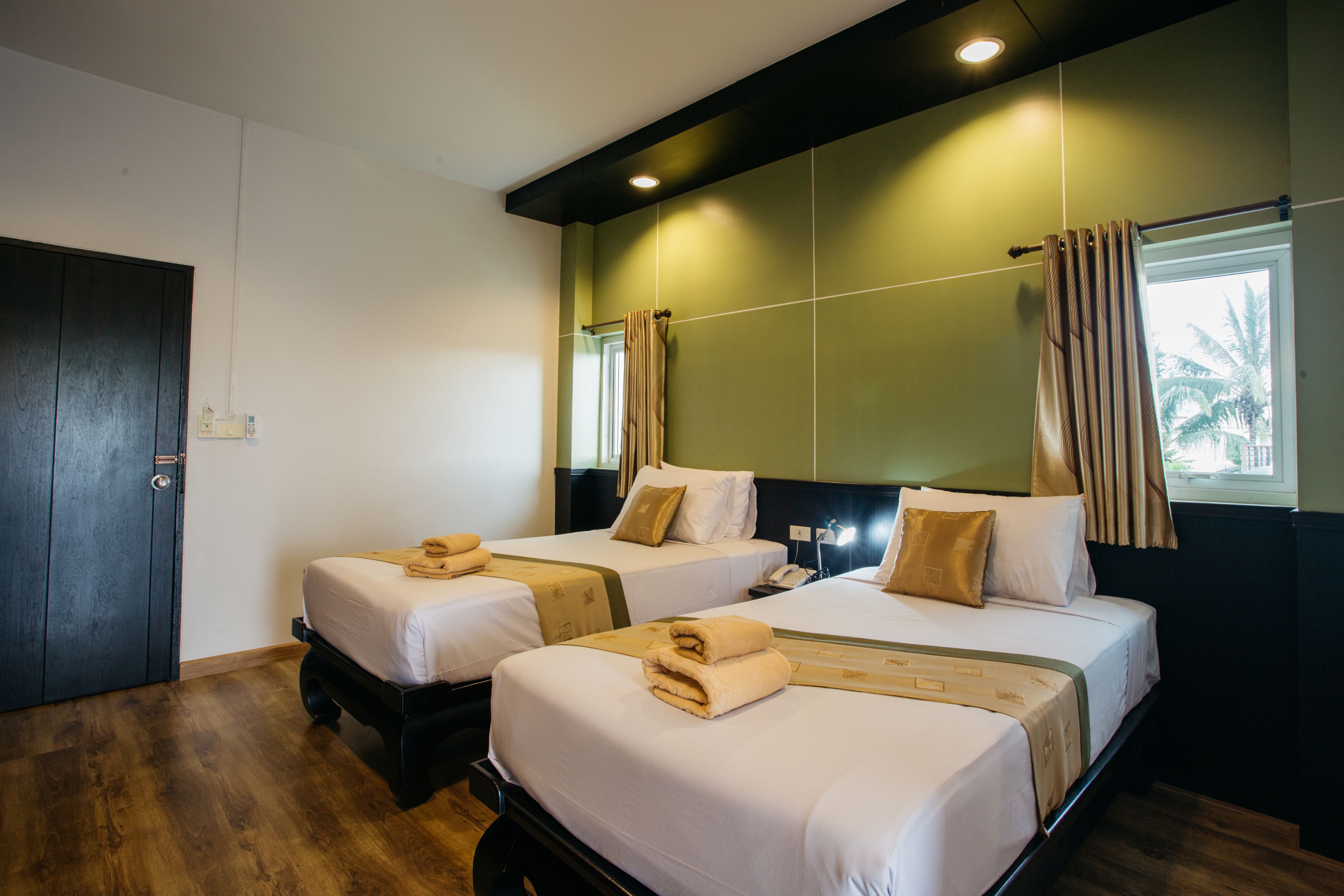 A hotel room with two beds, wooden flooring, a dark door, and a green accent wall.