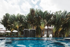 A swimming pool with lounge chairs and umbrellas, surrounded by large banana trees.