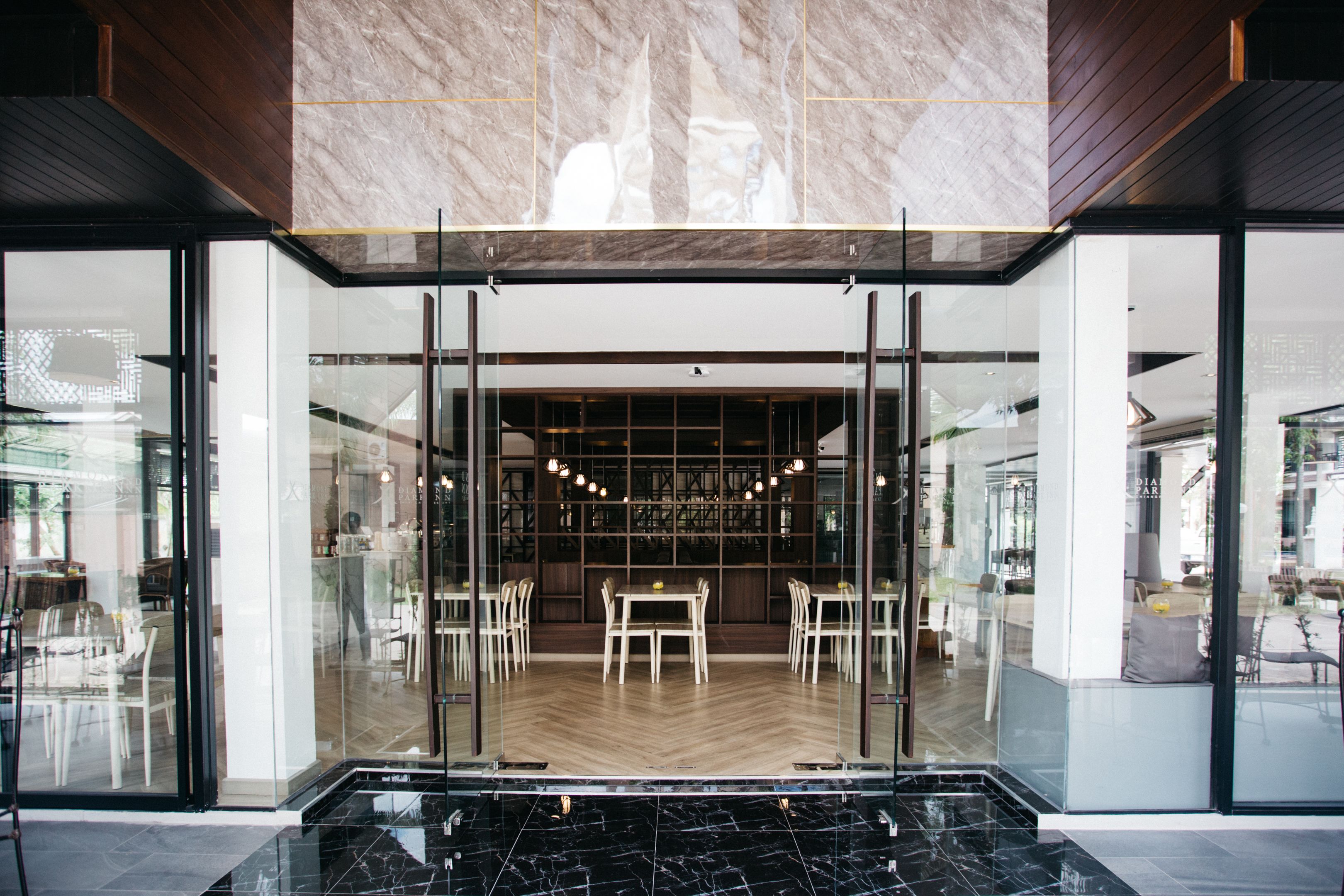 A modern restaurant with glass doors, a herringbone floor, and a central dining area with tables and chairs.