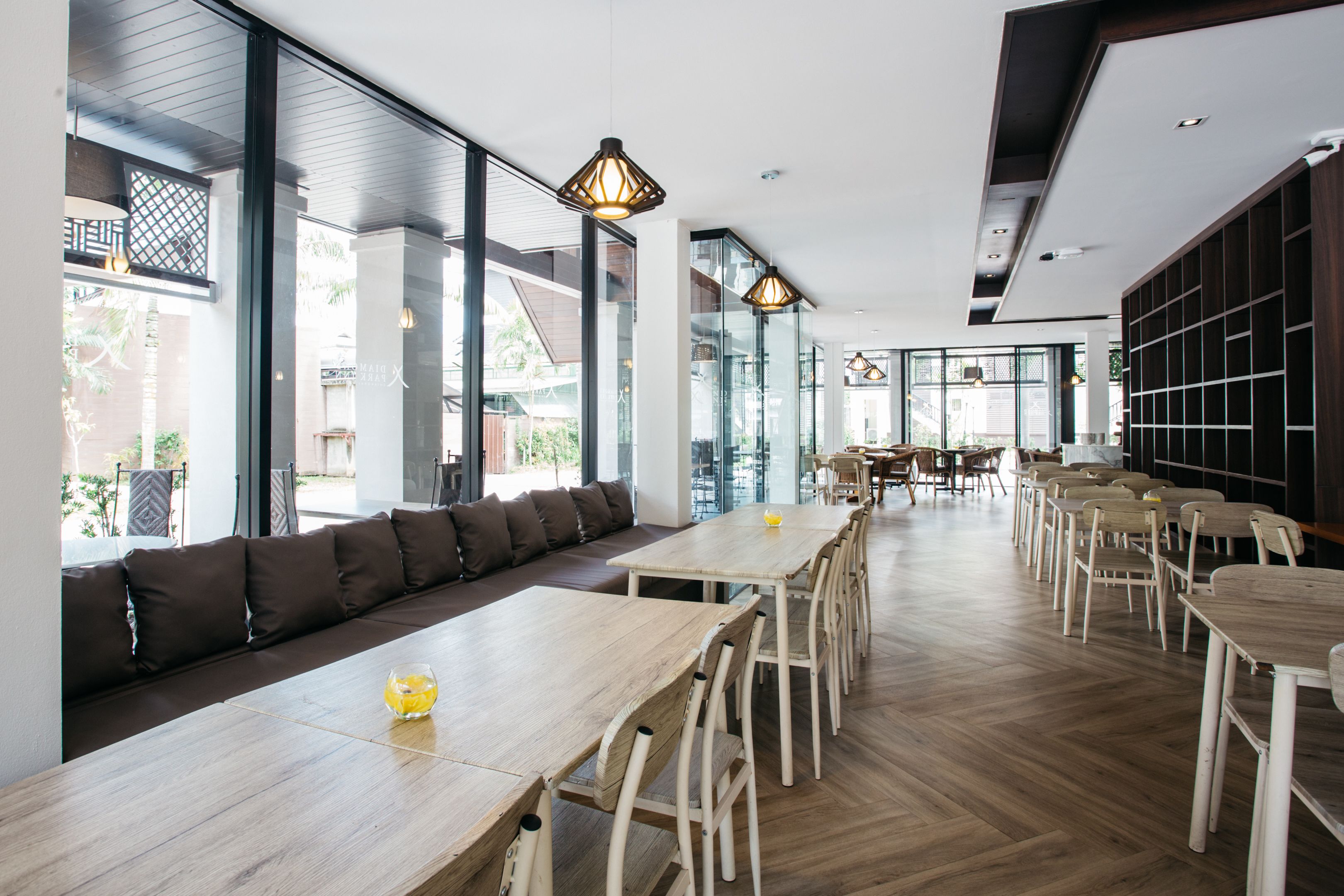 A modern dining area with long tables, chairs, and a seating area with cushions.