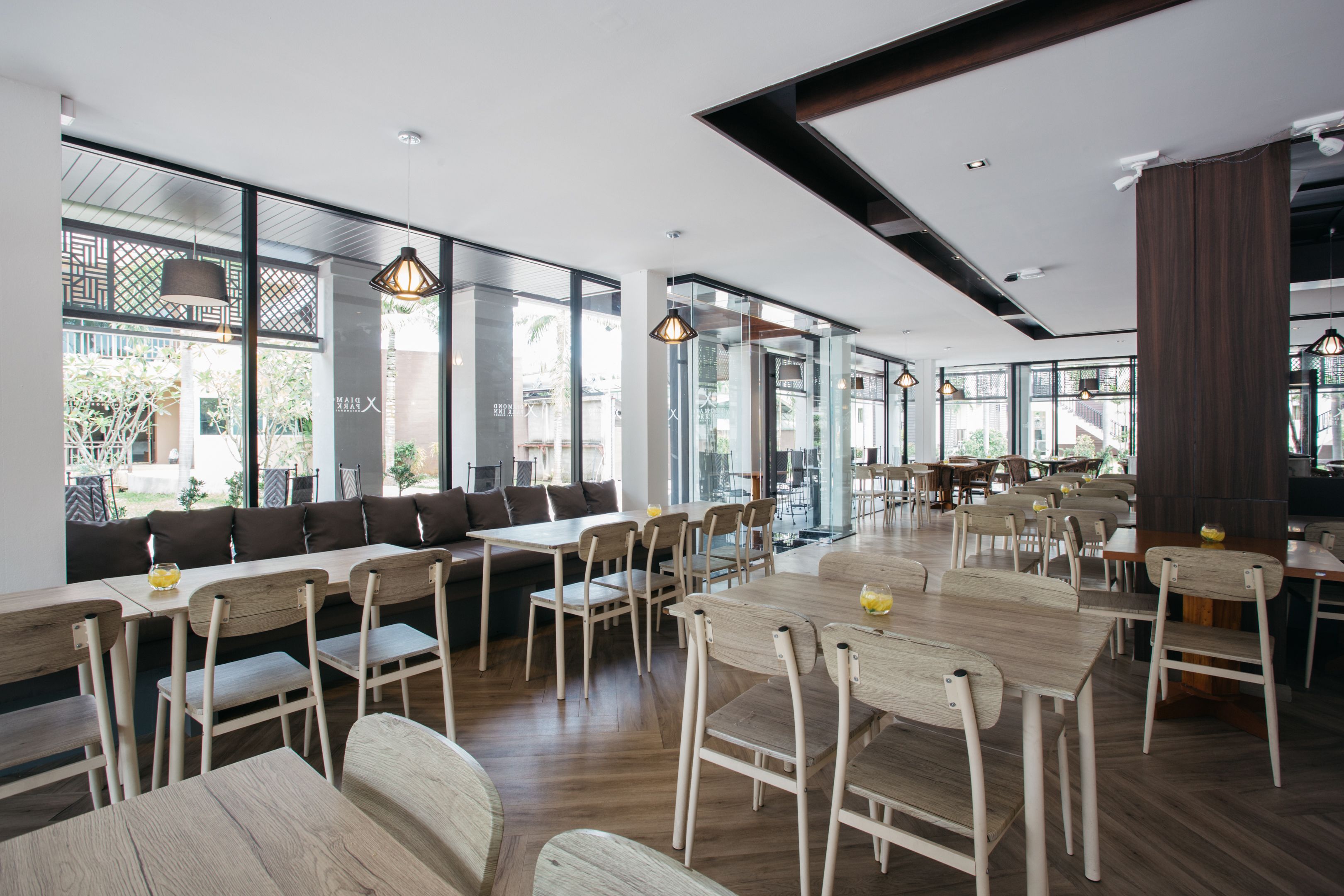 Un comedor moderno con mesas y sillas de madera, ventanas amplias e iluminación colgante.