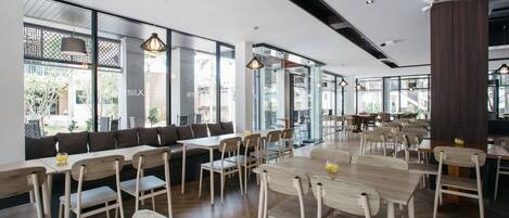 Un comedor moderno con mesas y sillas de madera, ventanas amplias e iluminación colgante.
