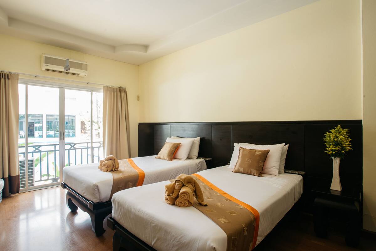 Habitación de hotel con dos camas, un ventanal con cortinas, un ventilador de techo y vistas a una piscina y un edificio.