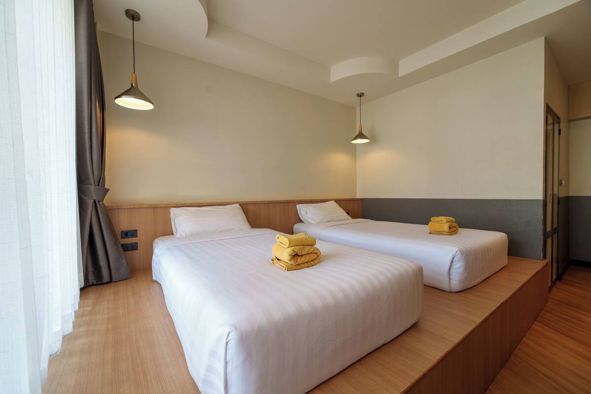 Habitación de hotel con dos camas, cabeceros de madera e iluminación colgante.