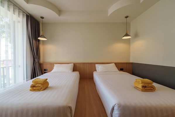 A hotel room with two beds, a large window with curtains, and two pendant lights.