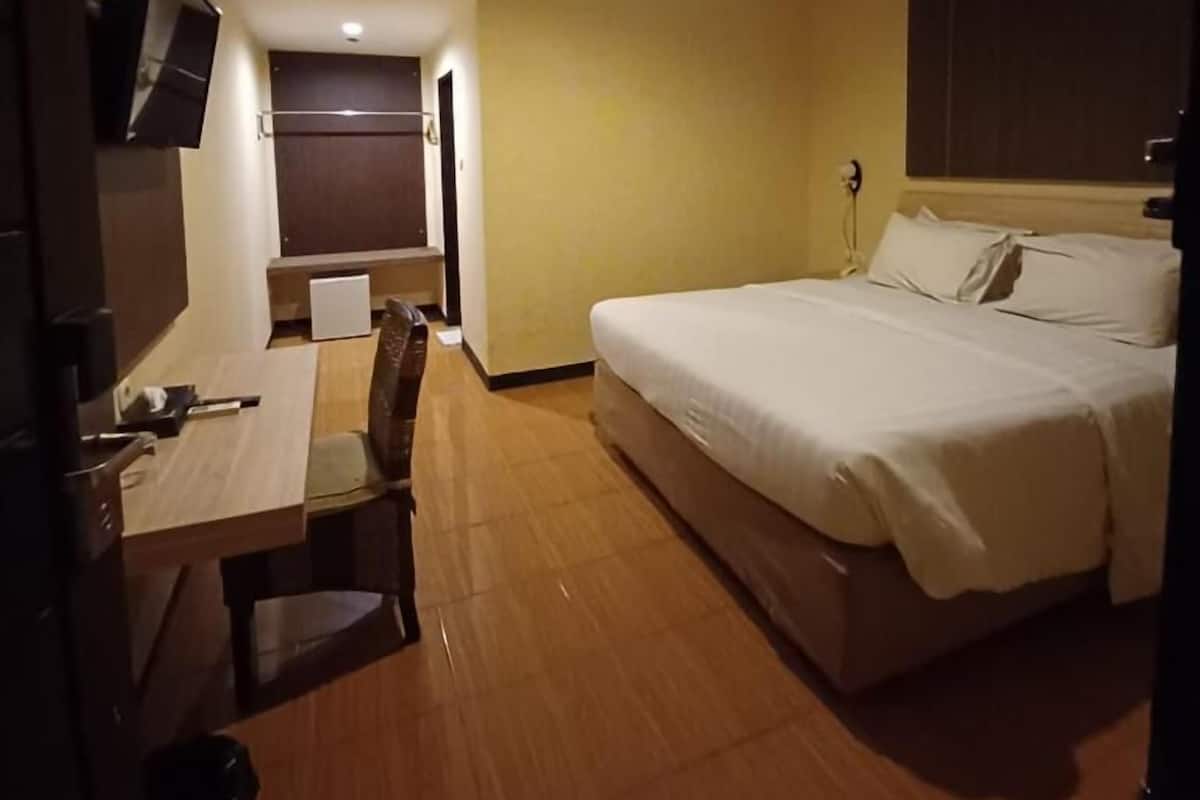 A hotel room with a bed, a desk, a chair, and a television.