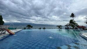 Piscina con tobogán, palmeras y vista al mar bajo un cielo nublado.
