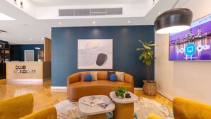 A modern hotel lobby with a reception desk, a sofa, yellow armchairs, a coffee table, and a TV screen displaying a cityscape. - Club Wyndham Perth, Trademark Collection by Wyndham (West Perth)