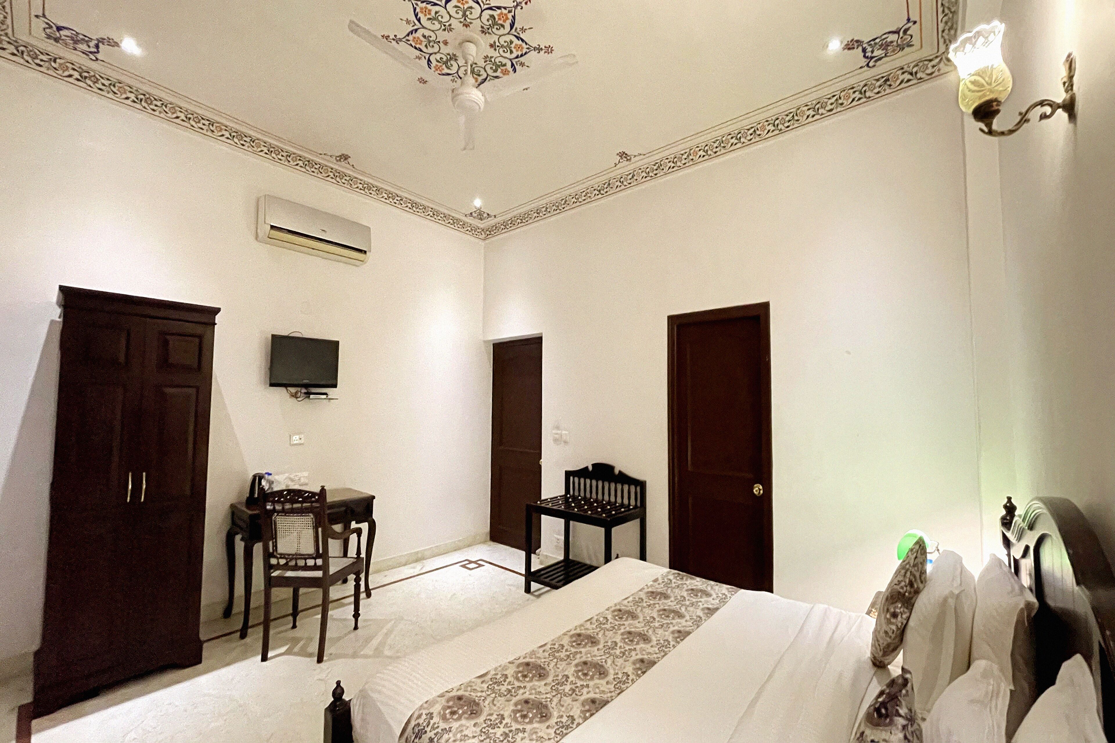 A hotel room with a bed, a desk, a chair, a television, and a wardrobe.