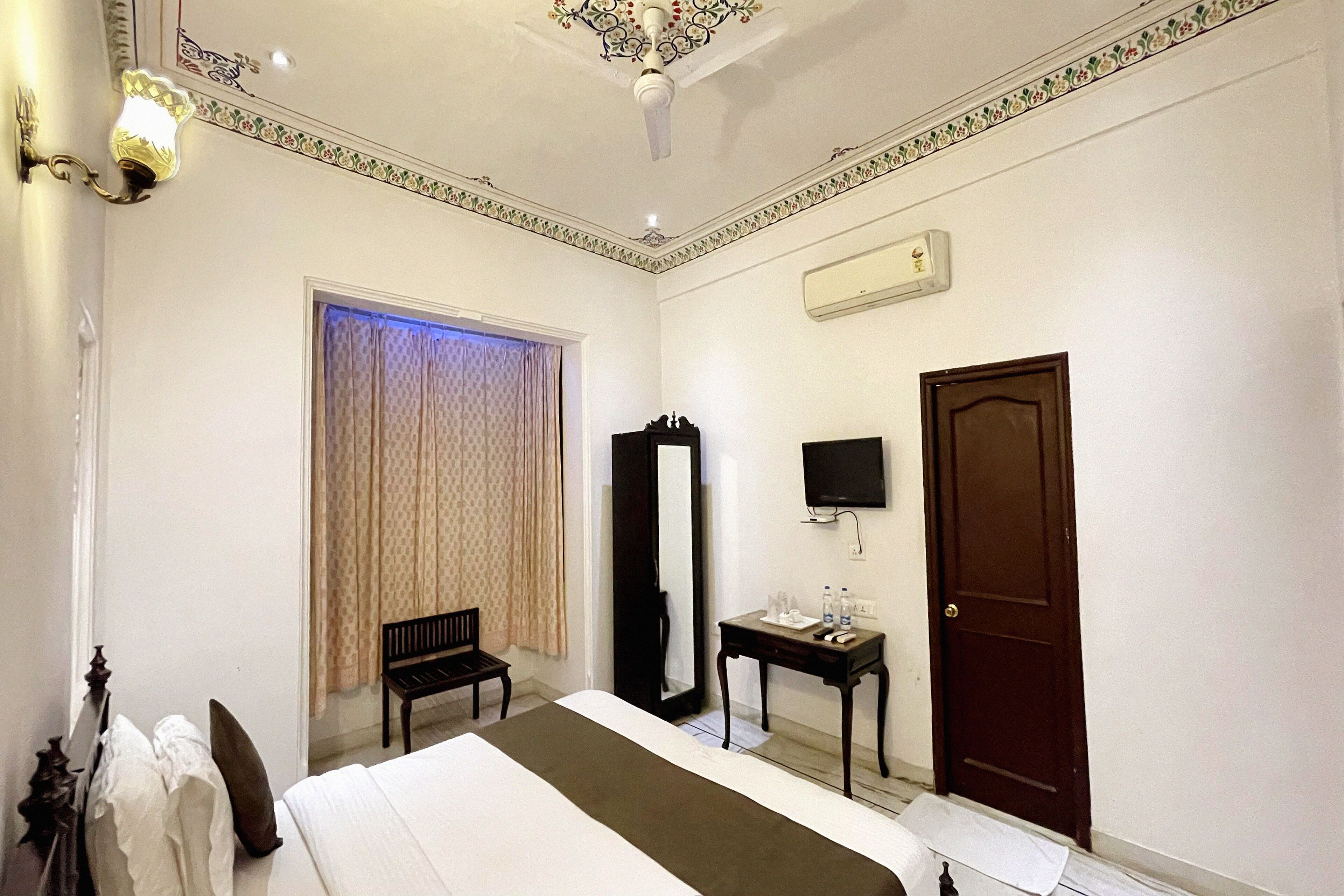 A hotel room with a bed, a desk, a chair, a television, and a door.