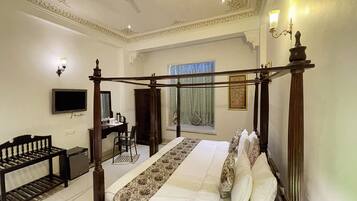 A four-poster bed with a canopy, a television mounted on the wall, a desk with a chair, and a window with curtains.