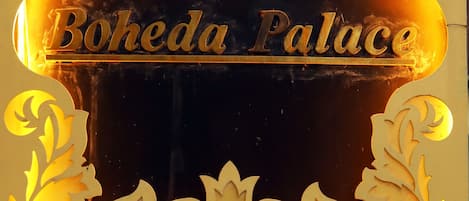 A sign for Hotel Boheda Palace with a decorative emblem and the name of a cafe and restaurant below.