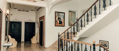 A grand staircase with ornate black railings and a wooden handrail, leading to a landing with a framed picture.